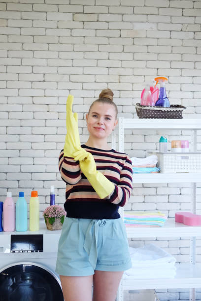 uśmiechnięta młoda kaukaska samica ubrana w żółte gumowe rękawiczki do czyszczenia prac domowych w loundry room. styl życia rodziny na koncepcji wakacje. - stereotypical housewife women domestic kitchen brown hair zdjęcia i obrazy z banku zdjęć