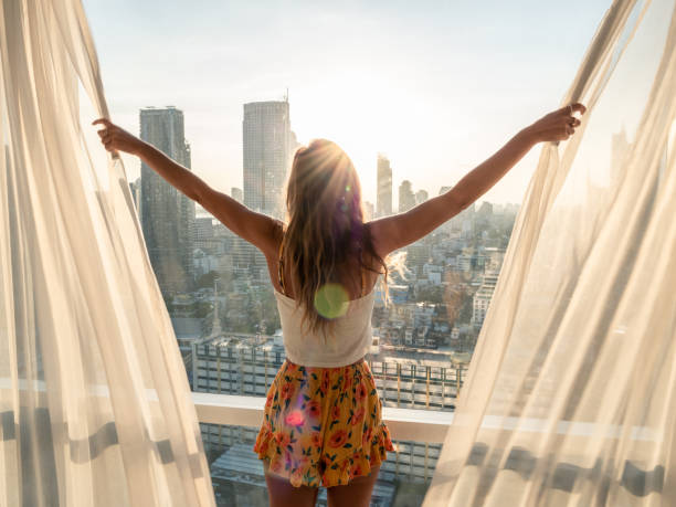 Woman opens curtains in bedroom room at sunrise Waking up in the morning, starting the day right. Sunrise over the city of Bangkok Morning stock pictures, royalty-free photos & images