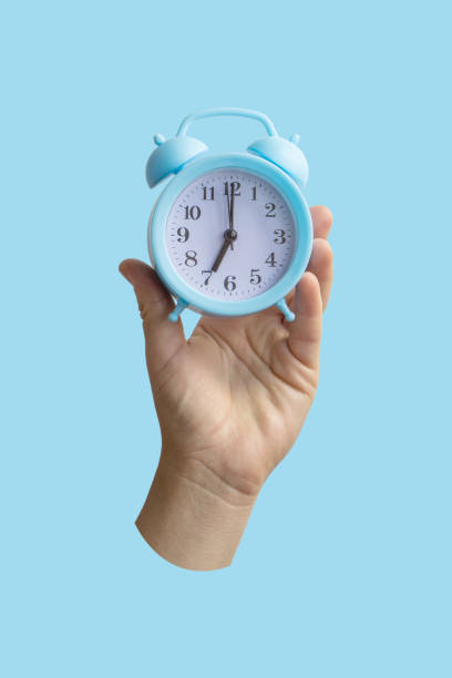 istock Female hand holding blue alarm clock on light blue background 1269682511