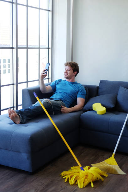 Lazy young Caucasian male relaxing with smartphone for online with community in social media on sofa in living room. He don't like doing housework. Lifestyle of Familyman on Holiday Concept. joven perezoso hombre caucásico relajante con teléfono inteligente para en línea con la comunidad en las redes sociales en el sofá en la sala de estar. no le gusta hacer las tareas domésticas. estilo de vida de familyman en holiday concept.