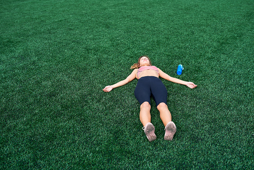 Sport and thin girl lies on a green field after training
