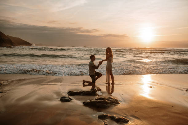 joven proponiendo a su novia en una playa - prometido fotografías e imágenes de stock