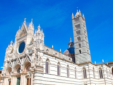 Siena’s masterpiece gothic cathedral which is of white marble captured against a beautiful blue sky. The picture highlights the majestic & artistic features of the cathedral.
