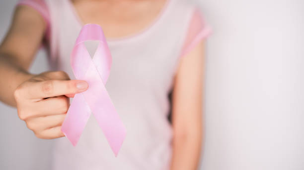 白いtシャツを着た女性は、白い背景、乳がんのシンボル、乳がん啓発月間のピンクのリボンを手に持っています。10月の重要な日 - breast cancer breast cancer awareness ribbon social awareness symbol human hand ストックフォトと画像
