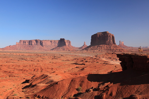 A woman riding on Horse  from John Ford's Point overlook in Monument Valley Tribal Park with the mittens and Merrick Butte in Arizona, USA
