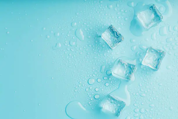 Ice cubes with water drops scattered on a blue background, top view. Refreshing ice.