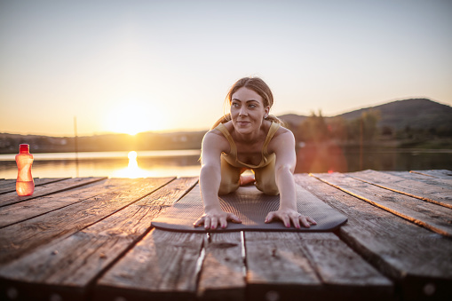 Photo of young woman practicing yoga on wooden pier at wild lake.
