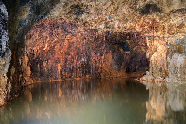 underground grotto in shades of red ochre with stalactites reflected in a small lake