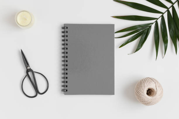 istock Top view of a grey notebook mockup with  workspace accessories and a palm leaf on a white table. 1269709000
