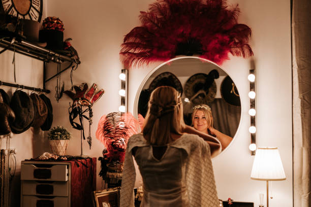 Beautiful theatre actress backstage Beautiful theatre actress backstage in front of the mirror in the changing room surrounded by theatre clothings and requisites (all are theatre mass products), creative color retouching with added noise theatre mirror stock pictures, royalty-free photos & images