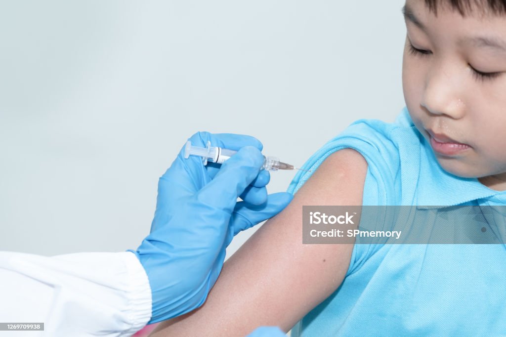 The doctor is using a syringe to vaccinate the Asian child's shoulder in hospital. Virus protection with vaccination concept. Vaccination Stock Photo