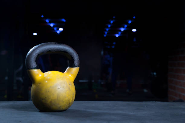 istock yellow kettlebell with black handle on black floor with gym background and bokeh lights low key dark lighting with copy space 1269710503