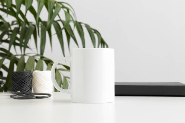 istock Mug mockup with workspace accessories on a white table and a palm plant. 1269713800