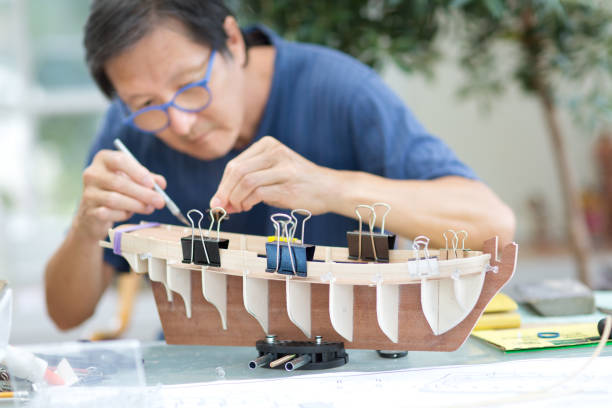 Retirement Hobby Leisure - Building Wooden Ship Kit Model Asian man retirement hobby of wooden model ship building. hull house stock pictures, royalty-free photos & images