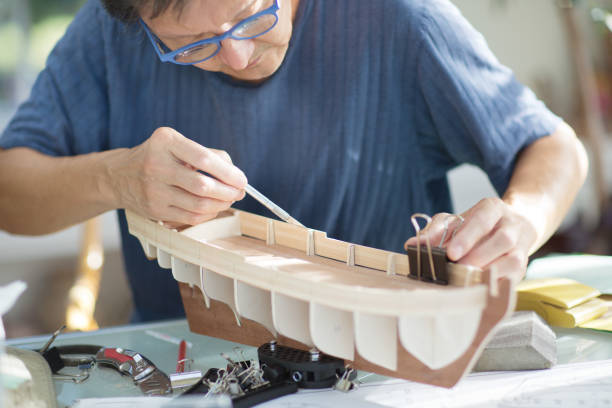 Asian man retirement hobby of wooden model ship building.