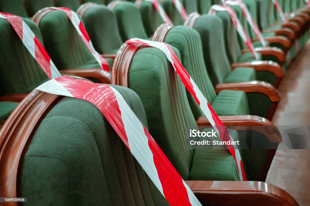 Background of empty seats in the cinema, theater, auditorium with a warning label. Presentation of a conference, opera, theatrical performance. Work during coronavirus, adhering to social distancing Keep your distance to avoid physical contact. Practice of social distancing. View of rows of seats marked with a warning tape in the cinema, theater, auditorium, conference hall. Protection COVID-19 Coronavirus Stock Photo