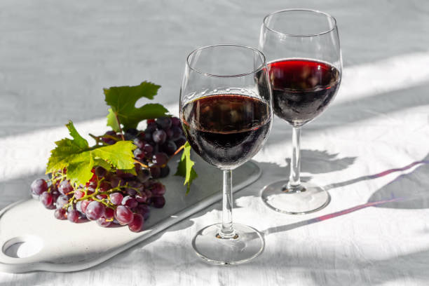 晴れた日に庭の白いテーブルの上に赤ワインと熟したピンクのブドウを持つ2つのワイングラス。 - 赤ワイン ストックフォトと画像