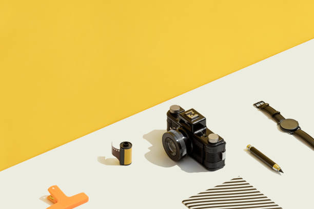 Photography flat lay on yellow and white background. Personal accessories with camera and film roll.
