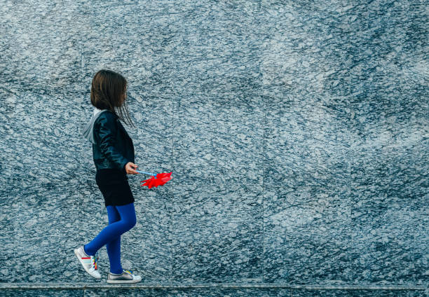 istock Little girl walking along a granite wall with red wind spinner 1269729460