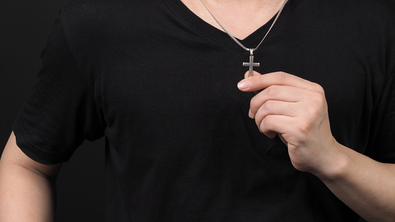Crucifix pendant or cross sign made from silver and hold in man hand. represent praying for someone that pass away from World pandemic coronavirus and close-up shot black background