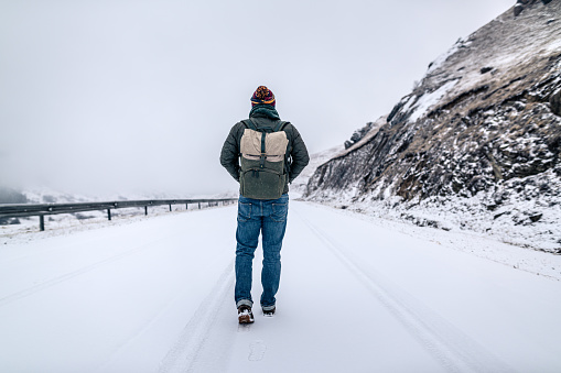 Man walks alone on an empty snowy road in mountains.