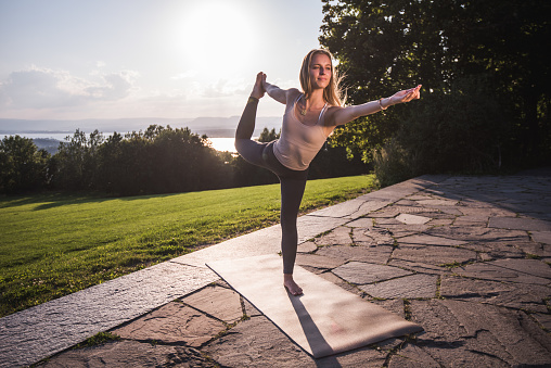 Attractive woman practicing yoga, stretching in Natarajasana exercise, Lord of the Dance pose, working out in nature.