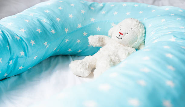 istock Light blue supporting pillow with stars on white sheet in bed for comfortable sleep of pregnant woman. Funny sleeping toy sheep, lamb. Goods, accessories for expectant mothers, kids, baby 1269737451