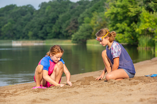 Side view of two young girls (sisters) playing in the sand at the beach on a summer day.