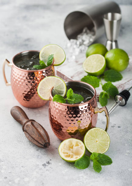 istock Moscow mule cocktail in a copper mug with lime and mint and wooden squeezer on light background with steel shaker and jigger 1269743245