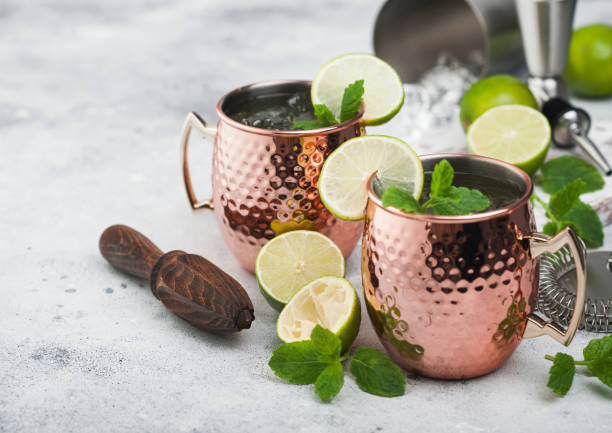istock Moscow mule cocktail in a copper mug with lime and mint and wooden squeezer on light background with steel shaker and jigger 1269743327