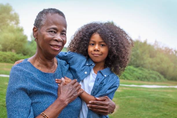 ritratto della nonna afroamericana che tiene nipote al parco pubblico - hand on heart immagine foto e immagini stock