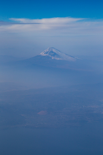 An aerial view looking down on Mount Fuji in the clouds. Some snow can be seen on the mountain. There is plenty of copy space for text around the mountain.
