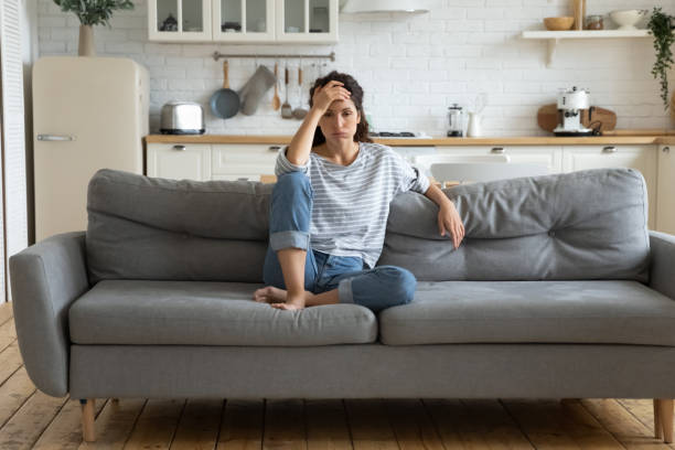 Tired upset woman worried about tiredness from domestic work. Tired upset woman worried about tiredness from domestic work sitting at couch. Frustrating mom stressful feels heaviness and headache at home. Fatigue parent trying relaxing in living room. irritation stock pictures, royalty-free photos & images