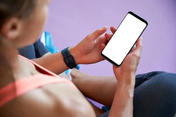 Photo of Fit sporty woman holding phone mock up white screen using fitness yoga app.