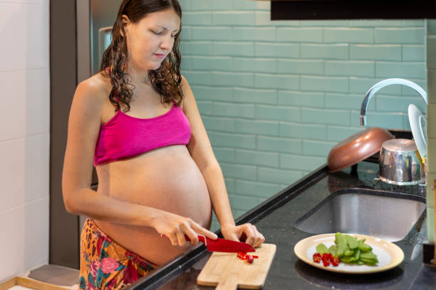 Pregnant woman cutting hot pepper on kitchen