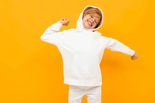 attractive blond boy in a white hoodie screaming out loud on an orange wall.