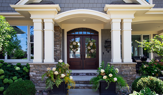 Front side of a home with a green wooden door and white stairs next to terrace with grass. A lamp is hanging in front of the door and patio is decorated with a small tree in a pot