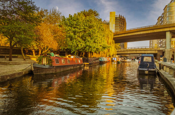 Autumn view of Regent's Canal in London, England, with boats and rising moon Autumn view of Regent's Canal in London, England at sunset with boats moored on both sides and buildings with rising moon in background regents canal stock pictures, royalty-free photos & images