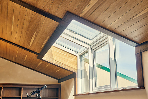 Attic interior with wooden ceiling and large window. Stargazing telescope