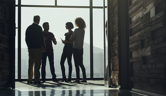 Shot of a group of businesspeople having a discussion while standing at a window in an office