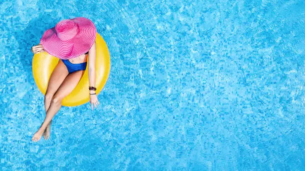 Photo of Beautiful woman in hat in swimming pool aerial top view from above, young girl in bikini relaxes and swims on inflatable ring donut and has fun in water on family vacation, tropical holiday resort