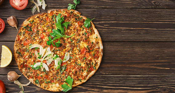 Turkish pizza lahmajun with minced lamb and beef on a thin crust with vegetables and herbs, horizontal layout. Wooden table, top view, flat lay, copy space