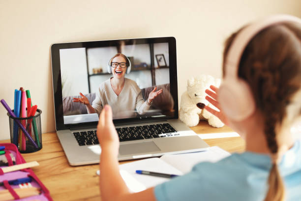 schoolgirl wearing headphones communicates via video link with an online teacher sitting at home schoolgirl wearing headphones communicates via video call with an happy online teacher sitting at home teacher classroom child education stock pictures, royalty-free photos & images