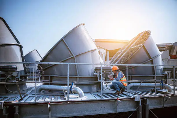 Photo of engineer under checking the industry cooling tower air conditioner is water cooling tower air chiller HVAC of large industrial building to control air system.