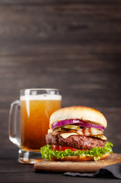 Homemade tasty burger with big beef, cheese, tomato, bacon and lettuce and lager beer mug. With copy space