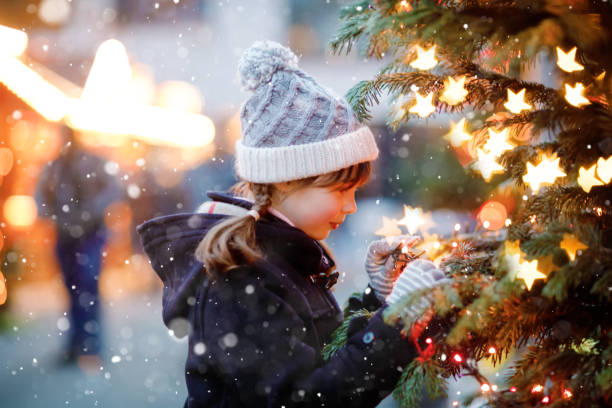 menina criança bonita se divertindo no mercado tradicional de natal durante a forte queda de neve. criança feliz desfrutando do tradicional mercado familiar na alemanha. estudante de pé perto de árvore de natal iluminada. - hot chocolate hot drink heat drinking - fotografias e filmes do acervo