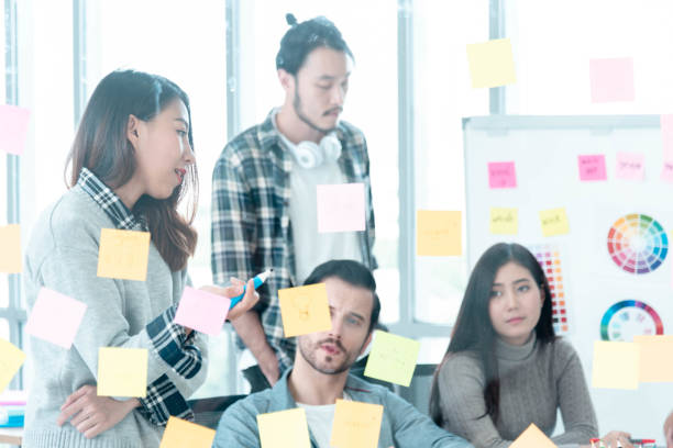 istock Diversity creative design team meeting using adhesive note planning strategy with business partners. Marketing teamwork working together in conference room. Multi-ethnic group brainstorming using note pad trust in team 1269809383