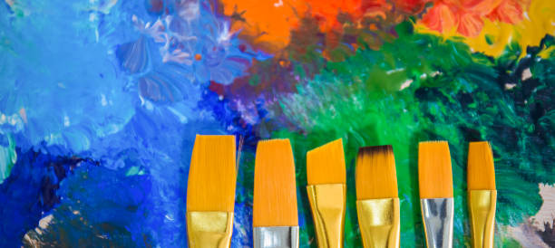 istock Acrylic or water color paint and brushes on wooden palette with copy space. Difference size of brushes over color paint background. Artist creative education concept banner 1269809473