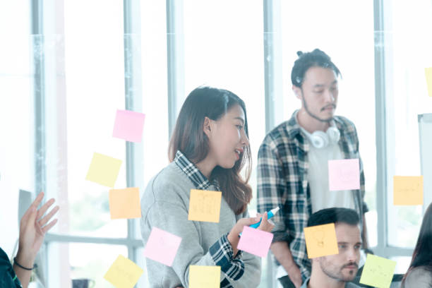 istock Diversity creative design team meeting using adhesive note planning strategy with business partners. Marketing teamwork working together in conference room. Multi-ethnic group brainstorming using note pad trust in team 1269809479