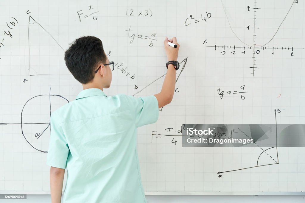 Schoolboy writing geometry equation Schoolboy in glass writing geometry equation on whiteboard, view from the back Mathematics Stock Photo